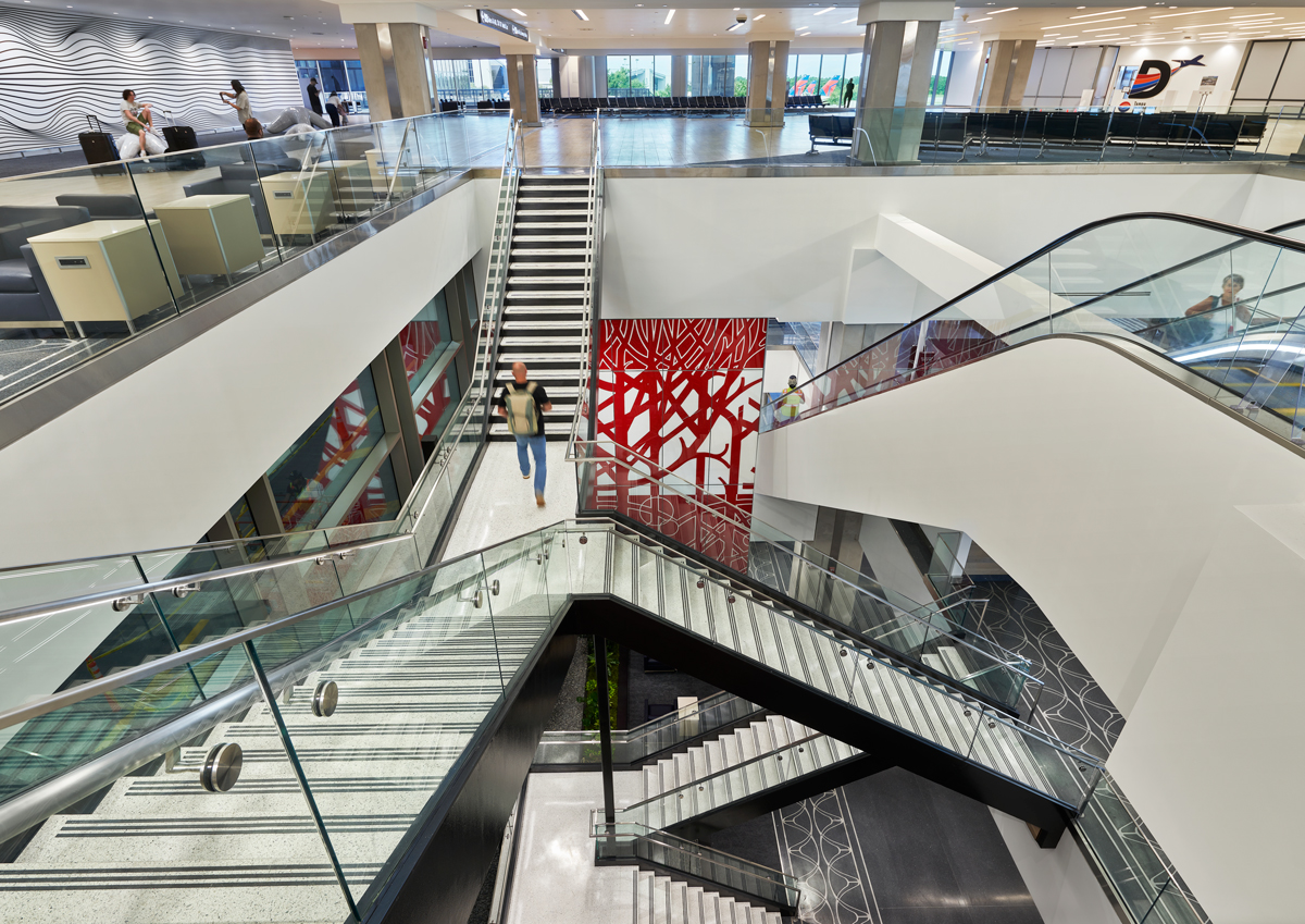 Multi-level interior view of Tampa International Airport showing stairways and escalators connecting the Express Curbsides to the main terminal, with open sightlines and integrated public art.