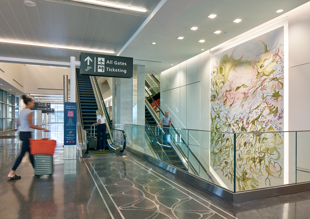 Interior view of Tampa International Airport’s Express Curbsides circulation area, showing escalators connecting to ticketing and gates alongside a large public art installation.