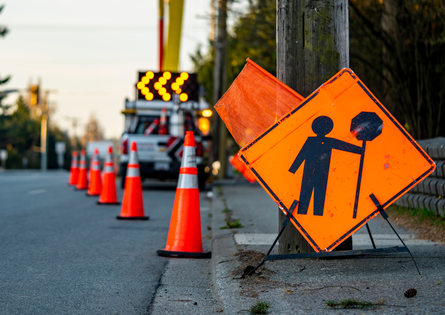 road closure with cones, signage and flags directing traffic to move over into left lane.