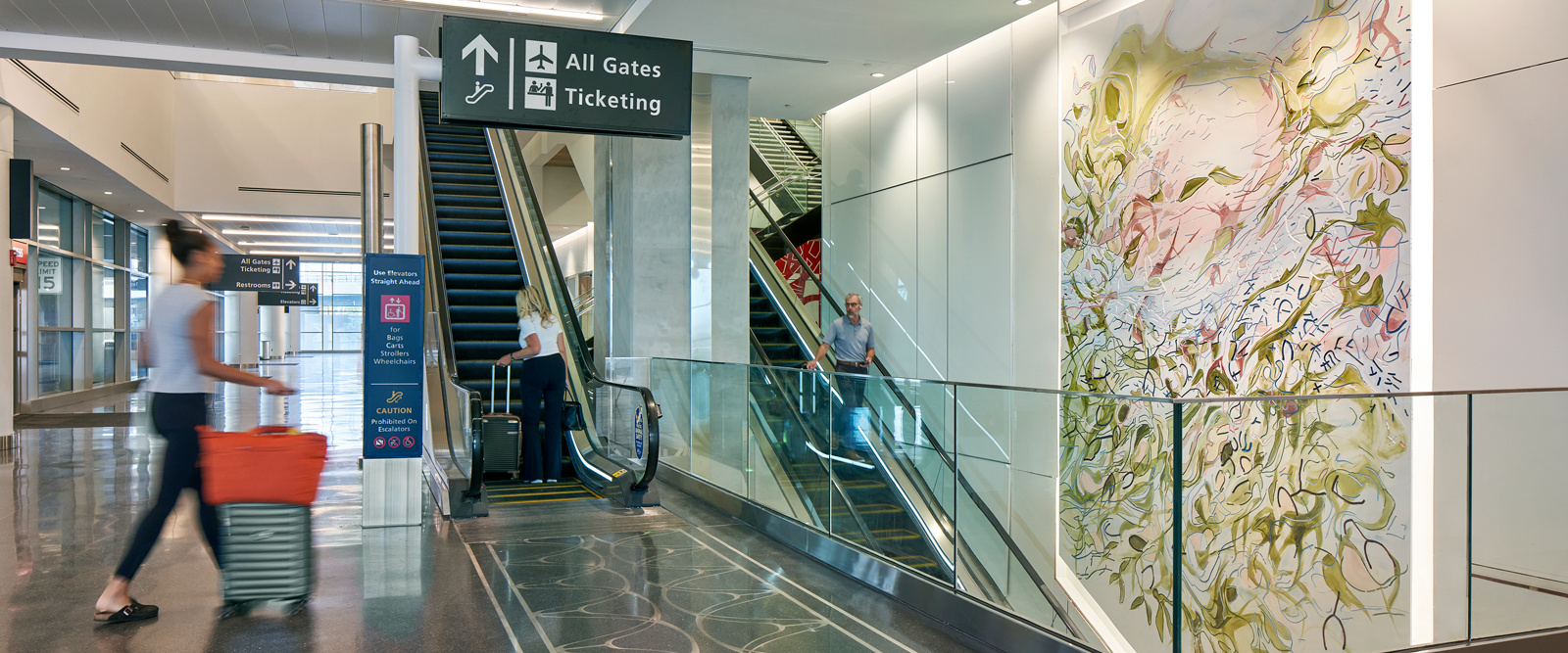 Interior view of Tampa International Airport’s Express Curbsides circulation area, showing escalators connecting to ticketing and gates alongside a large public art installation.