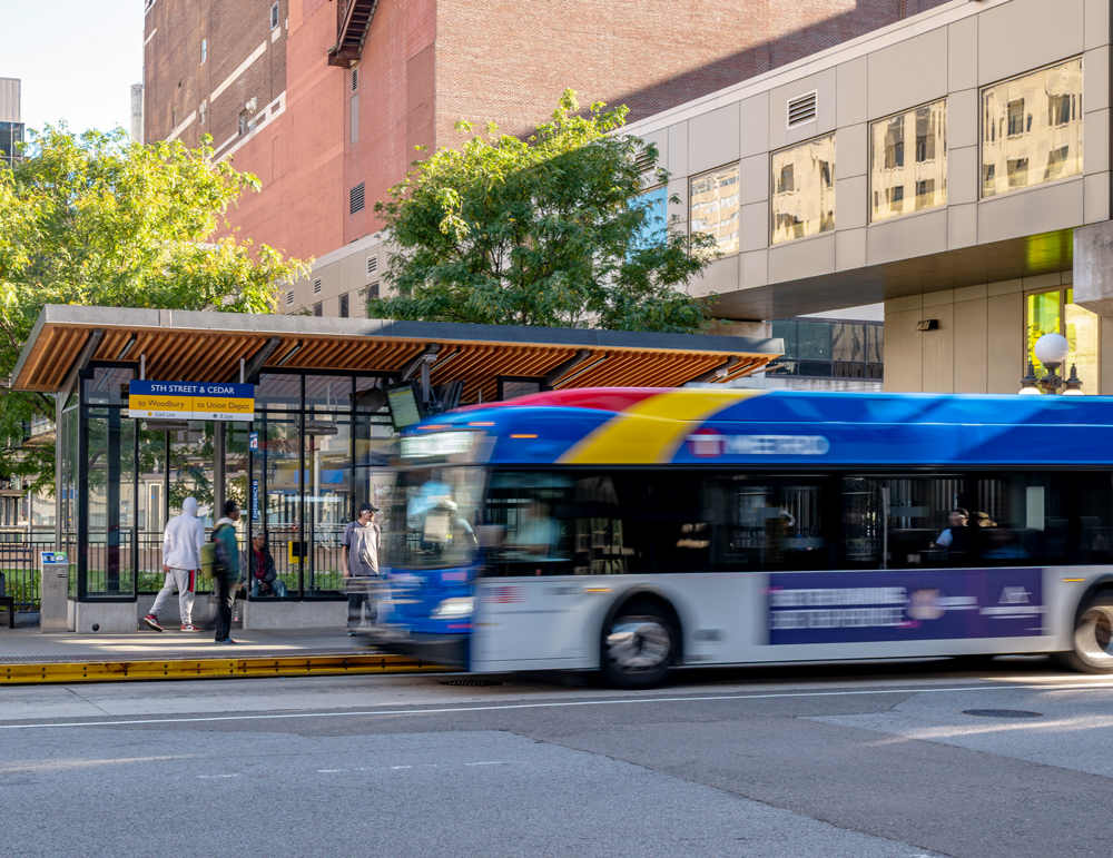 Metro Gold Line bus traveling past a downtown BRT station where riders wait on the platform.