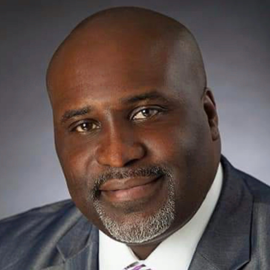 Headshot of Tremell Brown, deputy CEO of VIA Metropolitan Transit, wearing a gray suit and patterned tie, smiling slightly against a dark studio background.