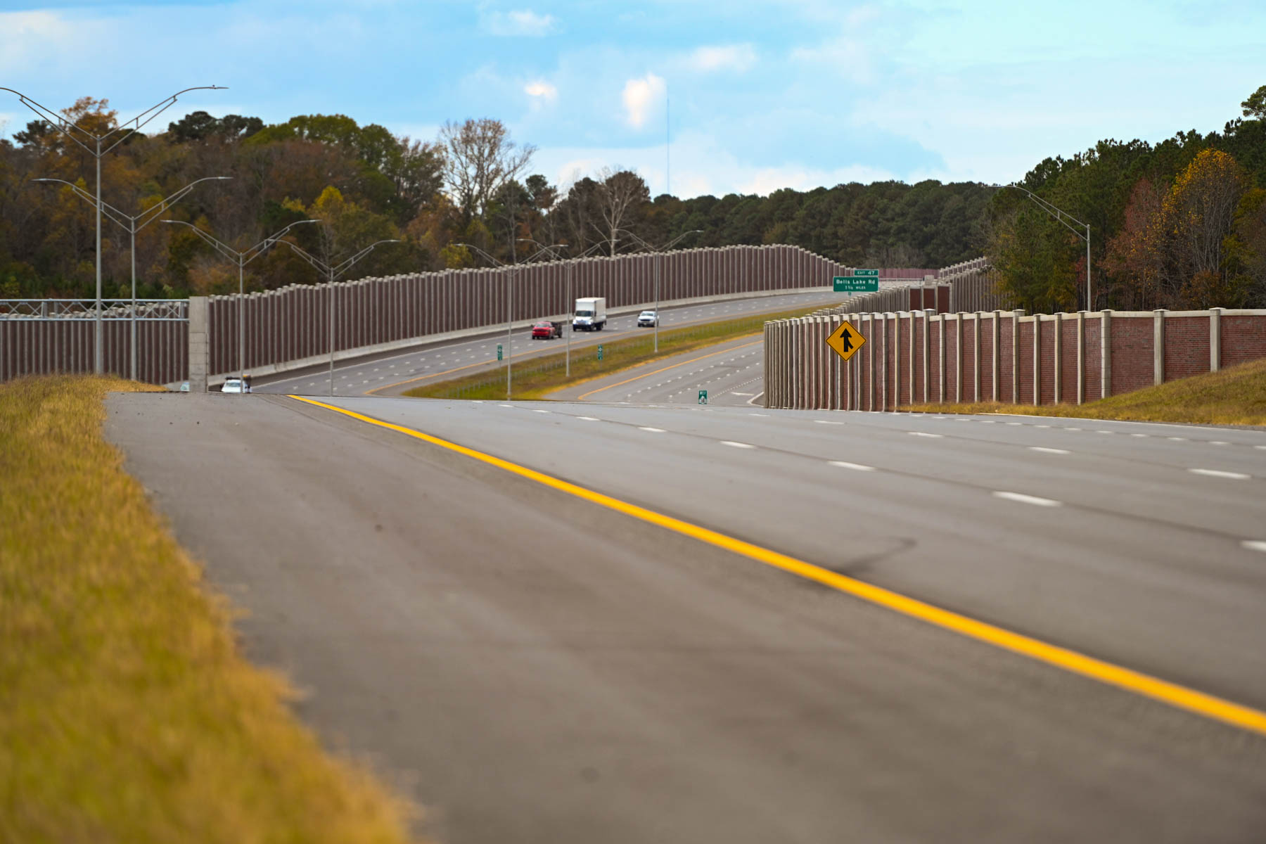 A wide view of the Complete 540 Phase 1 corridor showing a multilane highway bordered by tall sound walls with light traffic and a tree-lined backdrop.